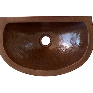 May include: A half-round copper sink with a hammered finish. The sink has a single drain hole in the center.