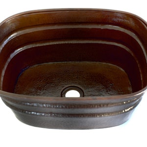 May include: A copper oval sink with a hammered finish and a drain hole in the center. The sink has a rustic, farmhouse style.