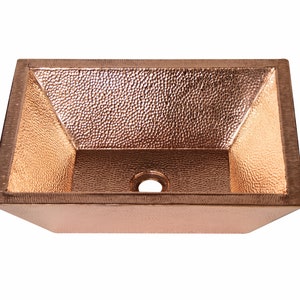 May include: A rectangular copper sink with a hammered finish. The sink has a square drain opening in the center.