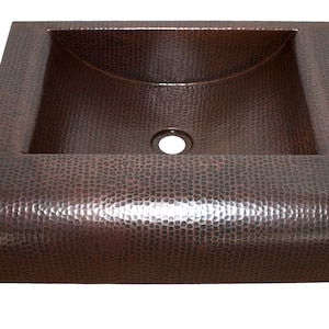 May include: A hammered copper vessel sink with a rounded front edge and a single drain hole. The sink has a square shape and a textured surface.