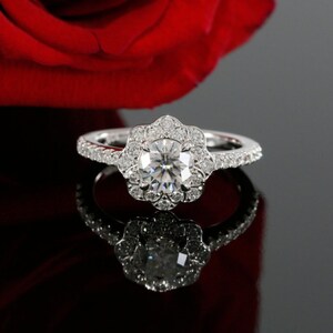May include: A silver engagement ring with a large, round, clear diamond center stone surrounded by smaller diamonds in a flower-shaped halo. The band is also set with smaller diamonds.