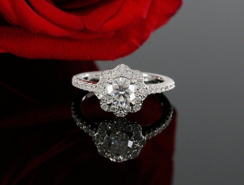 May include: A silver engagement ring with a large, round, clear diamond center stone surrounded by smaller diamonds in a flower-shaped halo. The band is also set with smaller diamonds.