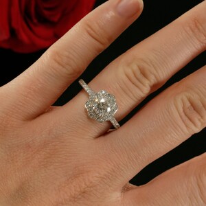 May include: A silver engagement ring with a round center diamond surrounded by smaller diamonds in a flower-shaped halo setting.