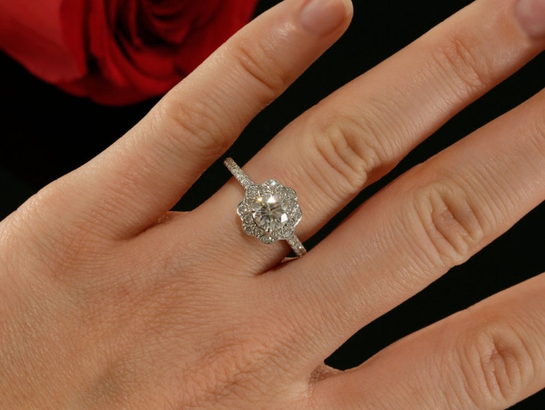 May include: A silver engagement ring with a round center diamond surrounded by smaller diamonds in a flower-shaped halo setting.
