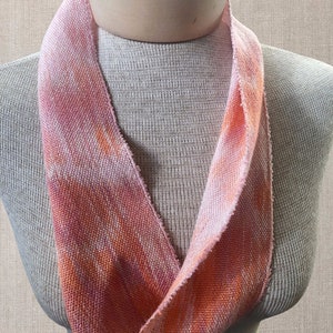 May include: A pink and orange woven fabric neck scarf. The scarf is folded in half and draped over a mannequin's neck.