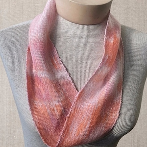 May include: A pink and orange hand-woven infinity scarf made of linen. The scarf is displayed on a mannequin.