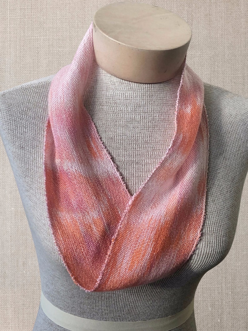 May include: A pink and orange hand-woven infinity scarf made of linen. The scarf is displayed on a mannequin.