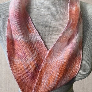 May include: A pink and orange woven infinity scarf with a soft, textured look. The scarf is displayed on a white mannequin.