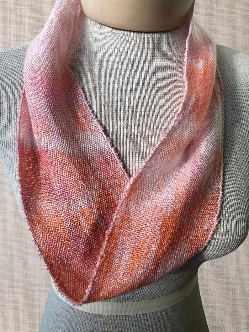 May include: A pink and orange woven infinity scarf with a soft, textured look. The scarf is displayed on a white mannequin.