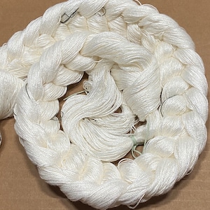 May include: A close-up of a white, braided embroidery floss. The floss is tightly wound and appears to be made of natural fibers.