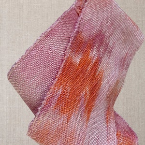 May include: A pink and orange woven fabric with a textured surface. The fabric is folded in half and has a frayed edge.