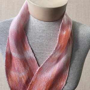May include: A pink and orange woven scarf with a textured pattern. The scarf is displayed on a mannequin.
