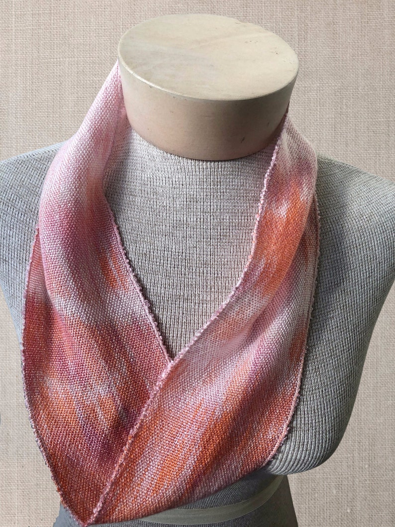 May include: A pink and orange woven scarf with a textured pattern. The scarf is displayed on a mannequin.
