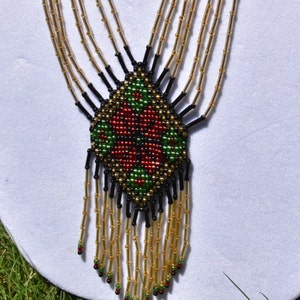 Puede incluir: Un collar de cuentas con un patr&oacute;n geom&eacute;trico en rojo, verde y negro. El collar tiene una franja de cuentas doradas.