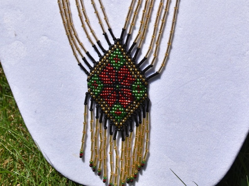 Puede incluir: Un collar de cuentas con un patr&oacute;n geom&eacute;trico en rojo, verde y negro. El collar tiene una franja de cuentas doradas.