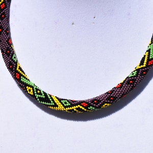 May include: A beaded necklace with a geometric pattern in shades of black, yellow, green, and red.