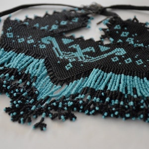 May include: A black and turquoise beaded necklace with a geometric pattern and fringe. The necklace is made of small beads and has a simple design.