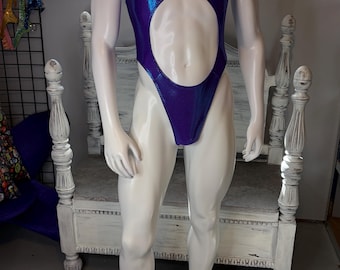 Puede incluir: Un body sin mangas de corte alto en tela morada metálica. La prenda presenta una gran abertura circular en el centro del torso, un escote redondo y una silueta ajustada que se extiende desde los hombros hasta la parte superior de los muslos.