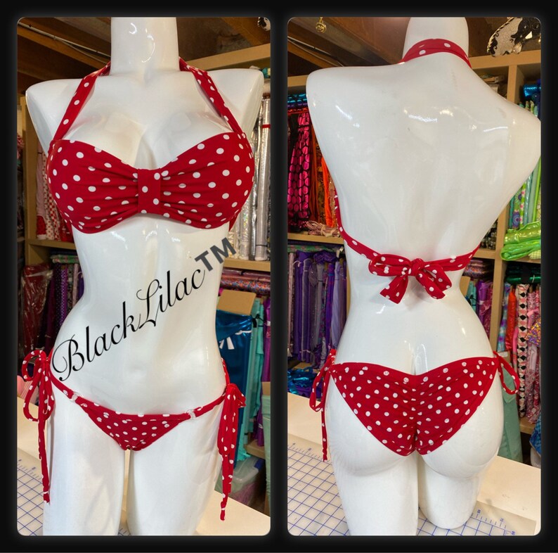 Puede incluir: Un bikini rojo con lunares blancos que presenta un top tipo halter con un detalle de nudo central y una braga de bikini a juego con lazos laterales. La prenda se muestra en un maniqu&iacute; blanco y el texto BlackLilac es visible a la izquierda.