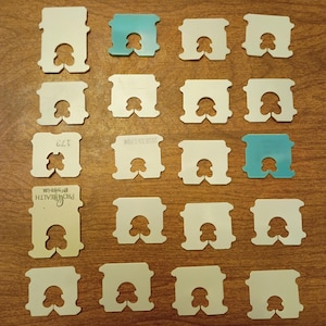 May include: A collection of twenty rectangular plastic bread clips arranged in a grid. Most clips are white, while two are teal. Each clip features a central U-shaped cutout. Some clips display printed text including ProHealth and Enviro-Lok.