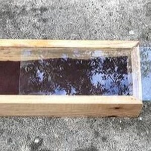 Pode incluir: Uma caixa de madeira com uma tampa de vidro, a tampa est&aacute; aberta e a caixa est&aacute; vazia. A caixa &eacute; feita de madeira natural e tem um aspecto r&uacute;stico.