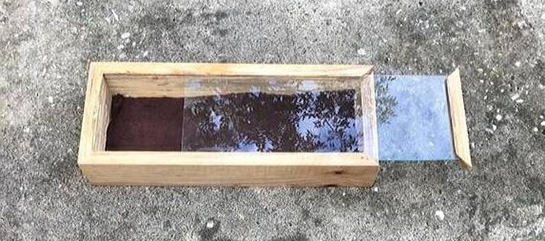 Pode incluir: Uma caixa de madeira com uma tampa de vidro, a tampa est&aacute; aberta e a caixa est&aacute; vazia. A caixa &eacute; feita de madeira natural e tem um aspecto r&uacute;stico.