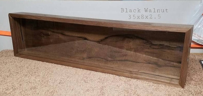 Pode incluir: Uma vitrine retangular longa feita de madeira escura com uma frente de vidro. A vitrine mede 89 cm de comprimento, 20 cm de largura e 6,4 cm de profundidade. A madeira tem um padr&atilde;o de gr&atilde;o natural e est&aacute; etiquetada como "Nogueira Negra".