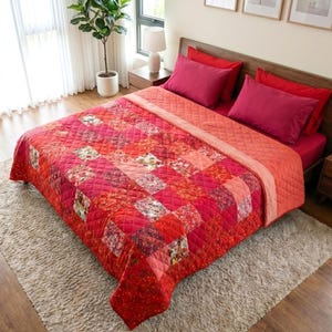 May include: A bed dressed with a vibrant red and pink patchwork quilt and matching pillows. The quilt showcases floral and geometric designs. The room is bright, with a neutral rug and wooden furnishings.