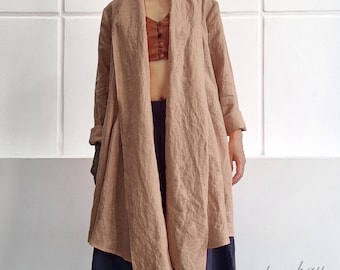 May include: A long-sleeved, open-front tan linen cardigan with a draped collar, paired with a rust-colored button-down crop top and wide-leg navy blue trousers. The garment features a textured fabric finish and a loose, flowing silhouette.