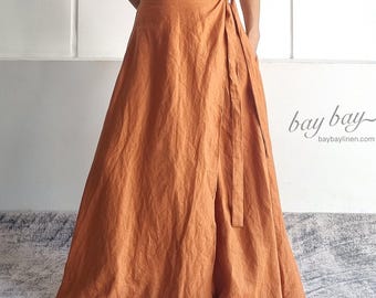 May include: A rust-colored two-piece set consisting of a cropped camisole top with a button-front closure and a matching floor-length wrap skirt with a side tie. The fabric has a visible linen-like texture. Text reads bay bay baybaylinen.com.