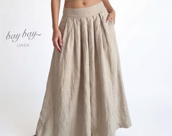 May include: A tan ribbed spaghetti strap crop top paired with a floor-length beige linen skirt featuring a wide waistband and deep vertical pleats. The text "bay bay LINEN" is printed in black on the left side of the image.