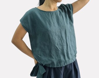 May include: A dark teal short-sleeved linen top with a round neckline and a side tie detail at the waist, paired with dark navy blue wide-leg trousers. The top features a loose fit and a textured fabric finish, with the brand name bay bay printed below.