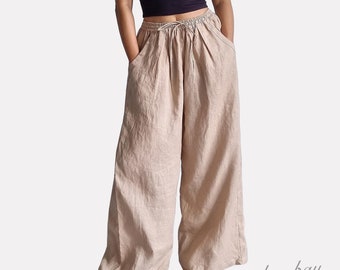 May include: A dark purple spaghetti strap tank top paired with wide-leg beige linen trousers. The trousers feature an elastic waistband with a drawstring tie and two side pockets. The bottom right corner displays the text bay bay baybaylinen.com.