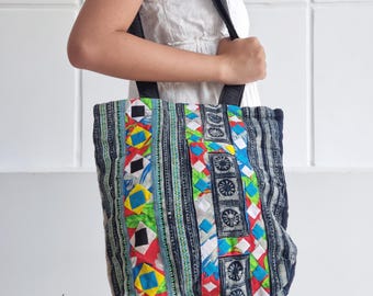 Peut inclure: Un sac fourre-tout coloré avec un motif patchwork. Le sac présente un mélange de motifs géométriques bleus, rouges, jaunes et verts. Il a des sangles noires et le texte "bay bay~ LINEN" est visible en bas à gauche.