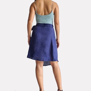 May include: A woman wearing a blue linen wrap skirt with a tie belt, a light blue tank top, and black heels. The skirt is knee-length and has a high waist.