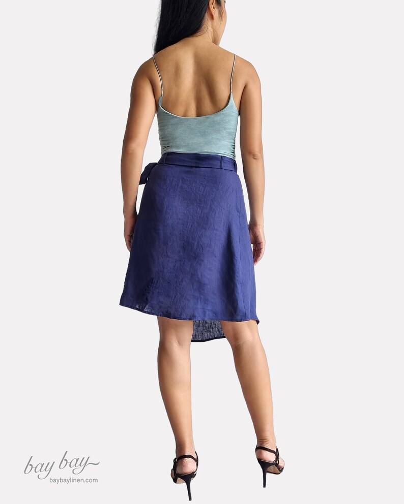May include: A woman wearing a blue linen wrap skirt with a tie belt, a light blue tank top, and black heels. The skirt is knee-length and has a high waist.