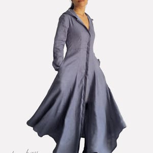 Puede incluir: Un vestido largo de lino con capucha de color azul claro. El vestido tiene un cierre de botones en la parte delantera y una falda ligeramente acampanada. La modelo lleva botas negras.