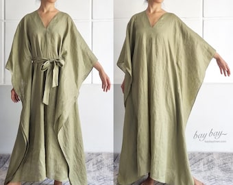 May include: A sage green kaftan dress with a V-neckline and wide kimono-style sleeves. The garment is shown in two variations: one cinched at the waist with a matching fabric tie belt and one loose-fitting. The text bay bay baybaylinen.com is visible.