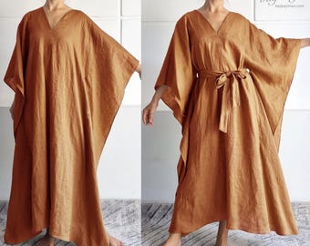 May include: A floor-length kaftan dress in a solid rust-brown color featuring a deep V-neckline, wide kimono-style sleeves, and a loose, flowing silhouette. The garment is shown both untied and cinched at the waist with a matching fabric tie belt.