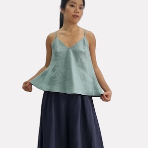 Op de afbeelding: Een vrouw draagt een lichtgroene linnen camisole top met dunne bandjes en een V-hals. De top wordt gecombineerd met een lange, marineblauwe linnen rok. De afbeelding is tegen een witte achtergrond.
