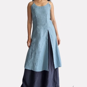 May include: A light blue linen dress with a front slit and a black linen skirt underneath. The dress has a scoop neck and thin straps.
