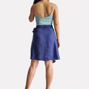 May include: A navy blue linen wrap skirt with a tie belt. The skirt is knee-length and has a flowy, A-line silhouette.