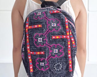 Peut inclure: Un sac à dos en jean foncé orné d'un motif coloré. Le motif comprend des détails roses, rouges, jaunes et bleus. Le sac à dos a des bretelles noires et le texte "bay bay~ LINEN" est visible.
