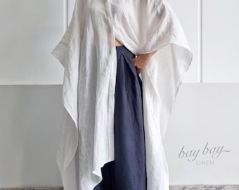 May include: A white oversized linen shirt with a classic collar and wide, flowing sleeves paired with dark navy blue wide-leg trousers. The garment features a button-down front and a loose, asymmetrical hemline. The text bay bay LINEN is visible.