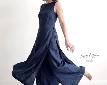 May include: A sleeveless navy blue jumpsuit featuring a round neckline and wide-leg trousers with high side slits. The garment is made of a textured fabric and includes the text "bay bay LINEN" printed in a dark script and block font.