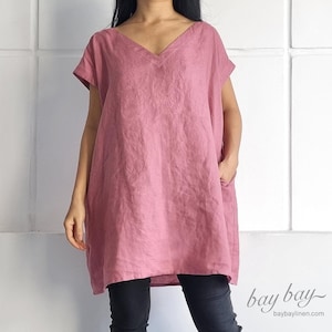 May include: A loose-fitting, dusty rose linen tunic with a v-neck and short sleeves. The tunic has a relaxed fit and falls to the mid-thigh.