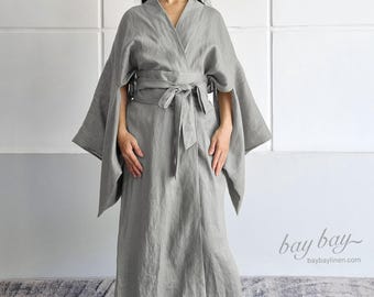 May include: A light gray robe featuring wide, kimono-style sleeves and a matching tie-waist belt. The garment has a V-neckline and a floor-length hem. The text "bay bay" and "baybaylinen.com" is printed in the lower right corner of the image.