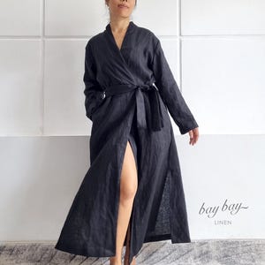 May include: A long, black linen robe with a wrap-around design and a matching belt. The robe has long sleeves and a high slit on one side. The text "bay bay~ LINEN" is visible in the lower right corner.