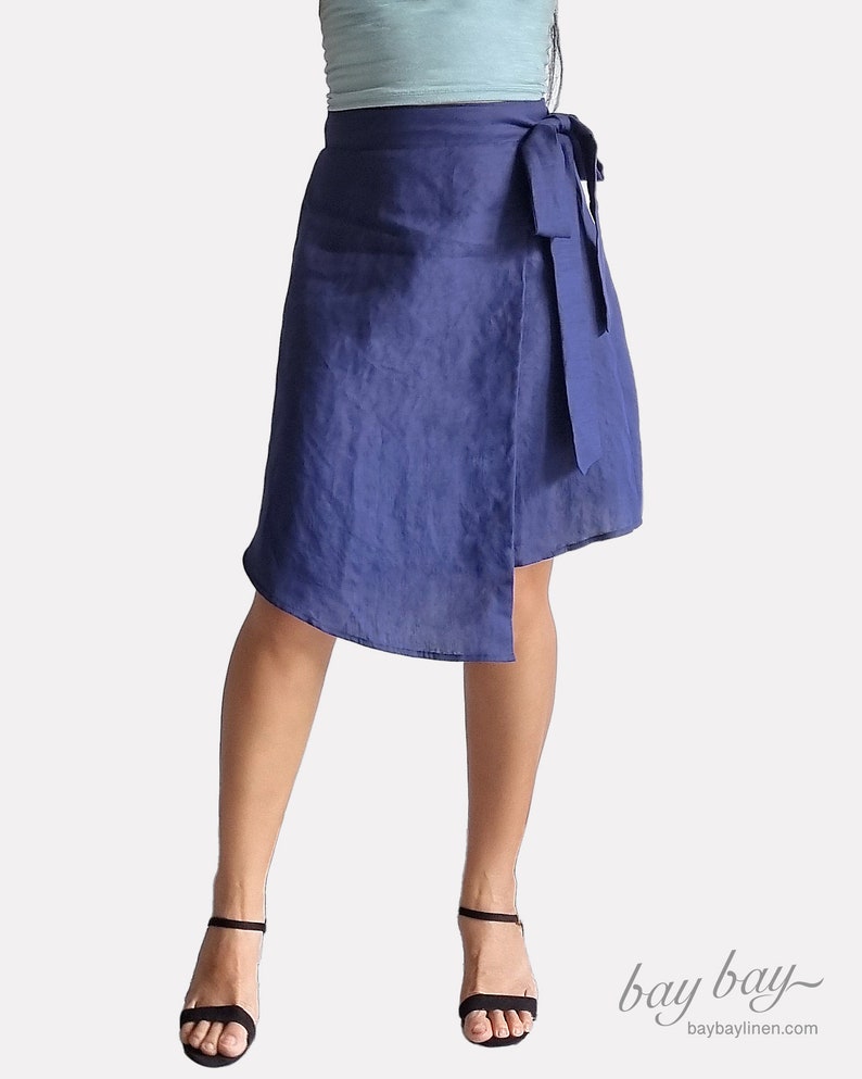 May include: A navy blue linen wrap skirt with a self-tie sash. The skirt is asymmetrical and falls to the knee on one side and above the knee on the other.
