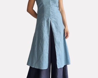 May include: A light blue sleeveless tunic with thin spaghetti straps, a deep V-neckline, and a long front center slit, worn over dark navy blue wide-leg trousers. The garment features a visible textured fabric finish throughout the entire set.